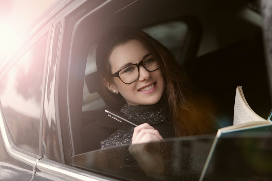 Smiling young woman reading a book in a car, enjoying leisure time during a sunny day.