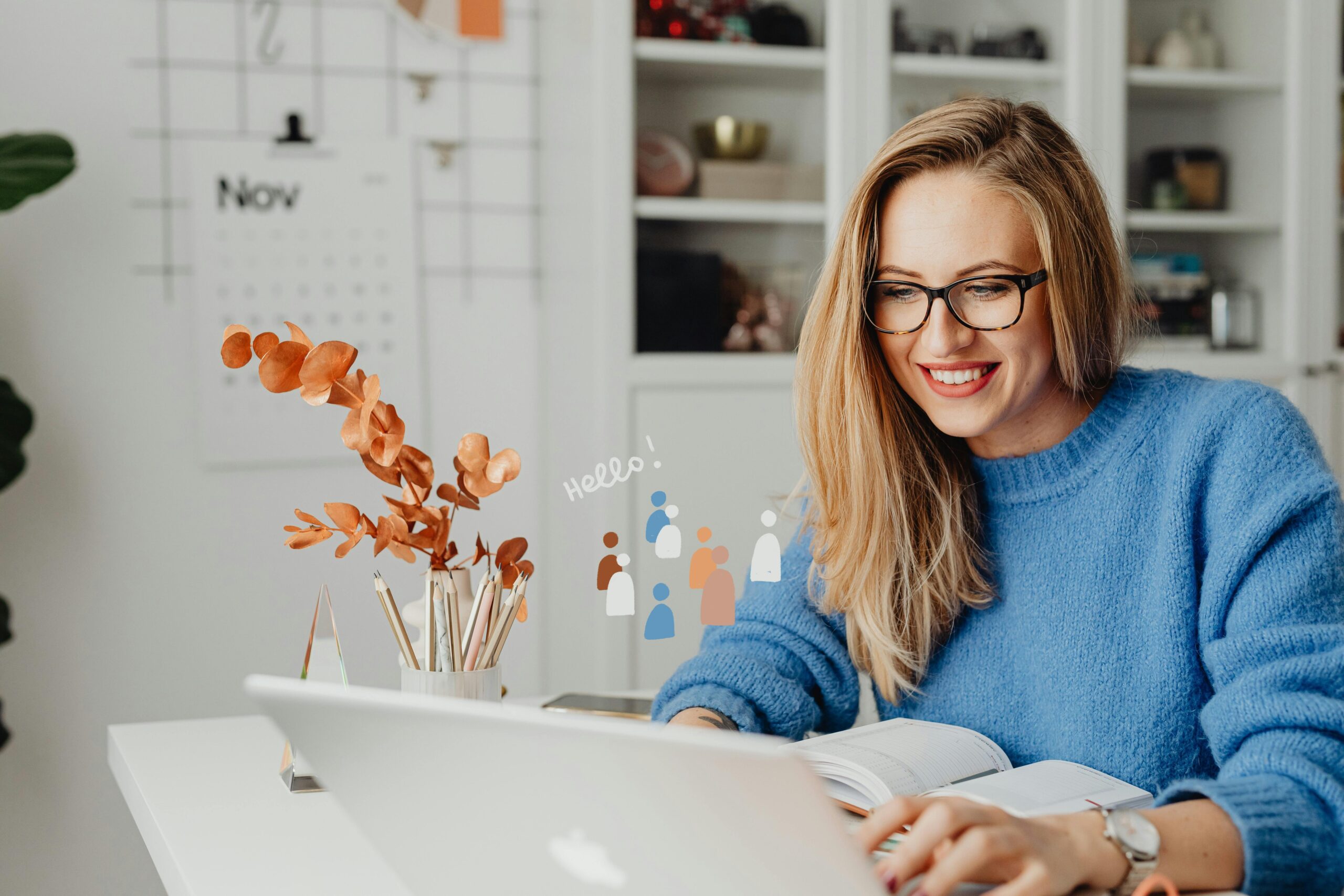Smiling woman in eyeglasses using a laptop at home office with decor and November calendar.